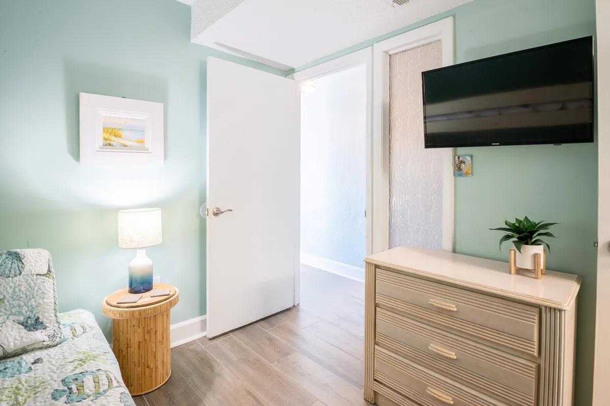 A bright and welcoming living room with a plush gray sofa (which converts to a queen sleeper), a lamp, dresser, TV, and wall art. The room is both functional and stylish, offering flexible space for additional guests.