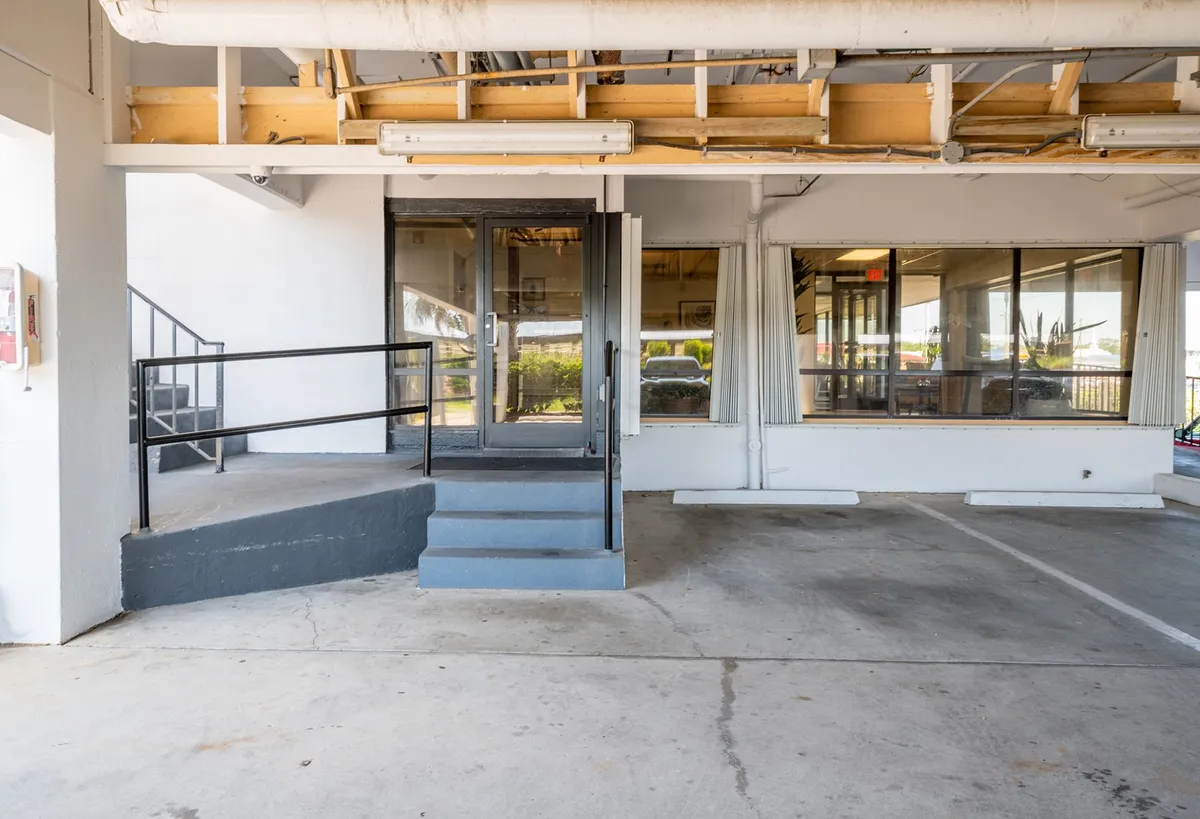 This exterior image showcases the entrance stairs leading up to a welcoming entryway, with large windows and an exposed ceiling hinting at a bright, open atmosphere inside. The scene suggests a space accessible for gatherings and events, with a community-oriented feel.