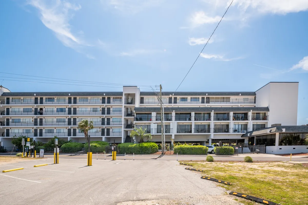 This exterior shot shows the building’s inviting facade framed by palm trees, with the parking lot and a glimpse of courtyard seating. The scene conveys a relaxed, welcoming environment, hinting at the convenience and comfort of the home base for local adventures.