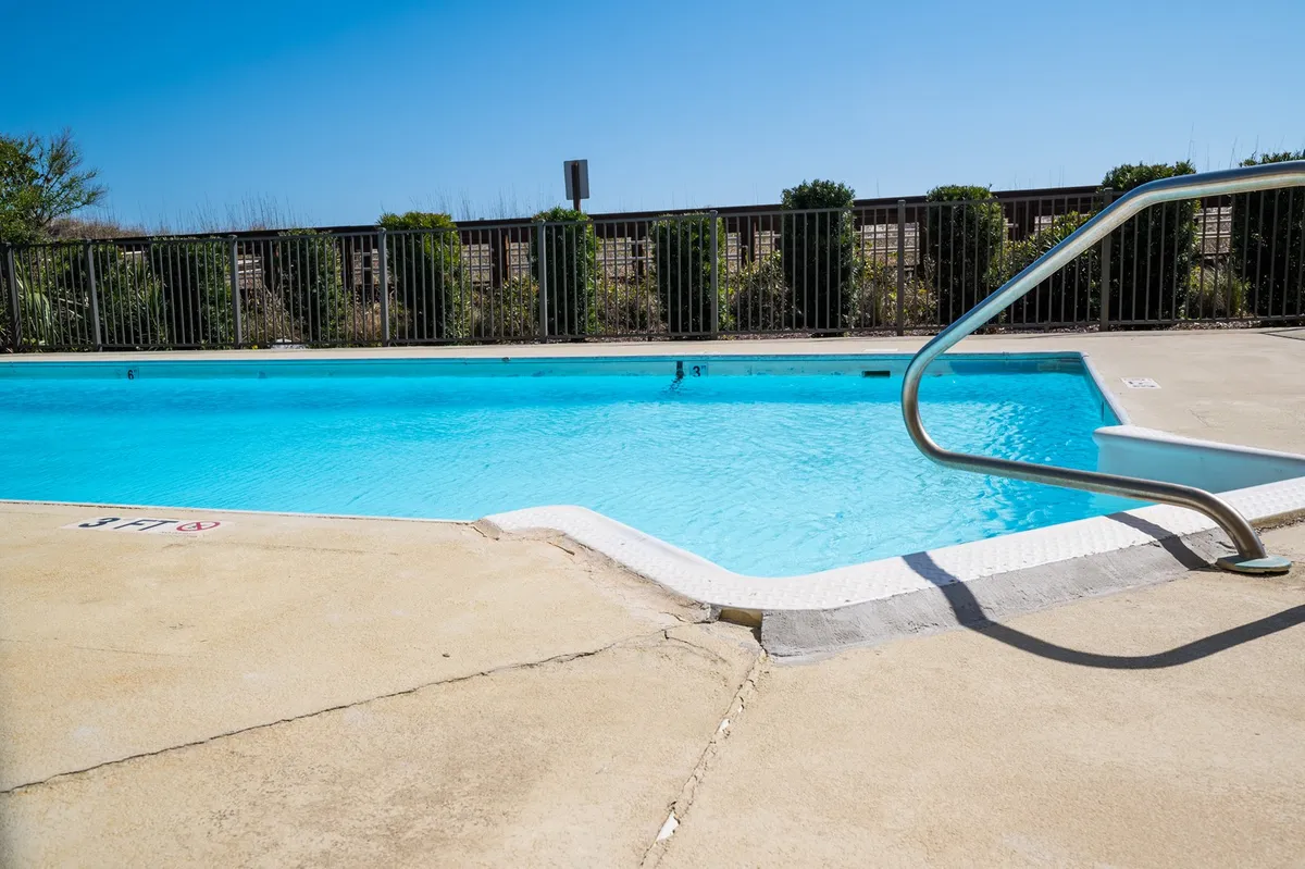 A sparkling oceanfront swimming pool bordered by a poolside railing, with clear blue water inviting guests to swim or sunbathe. The pool is set against the backdrop of open sky, creating a vibrant, resort-style atmosphere. Lounge chairs and subtle greenery enhance the space, suggesting a spot for both relaxation and social gatherings.