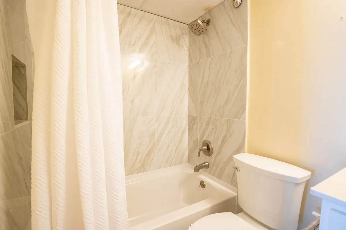 A tranquil bathroom featuring a bathtub with a shower curtain and a toilet, designed for both relaxation and convenience. The setting is clean and inviting, suitable for refreshing showers or unwinding in a bath.