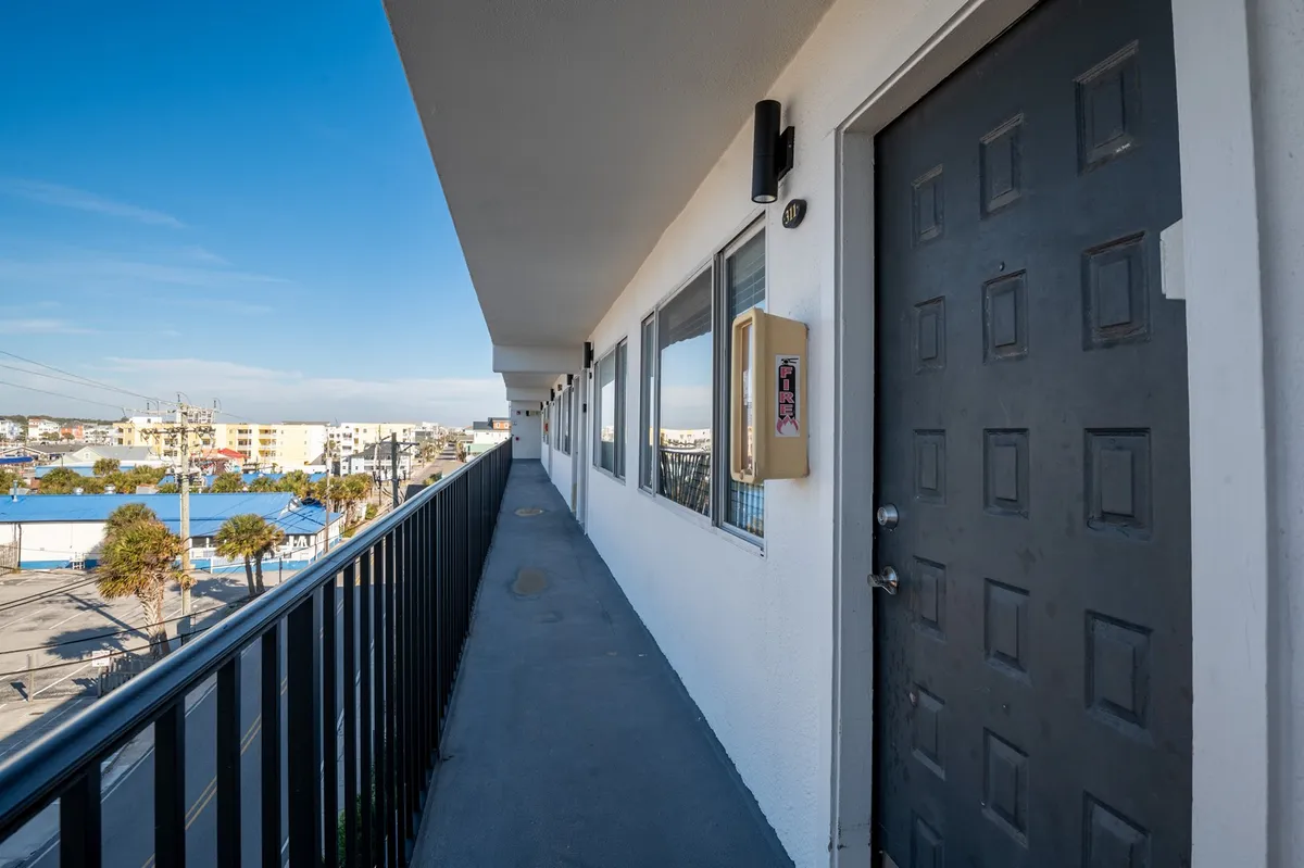 An exterior shot featuring a doorway, balcony railing, and windows, with space for guests to socialize outdoors. The casual mood suggests relaxing with friends and watching sunsets before heading into town.