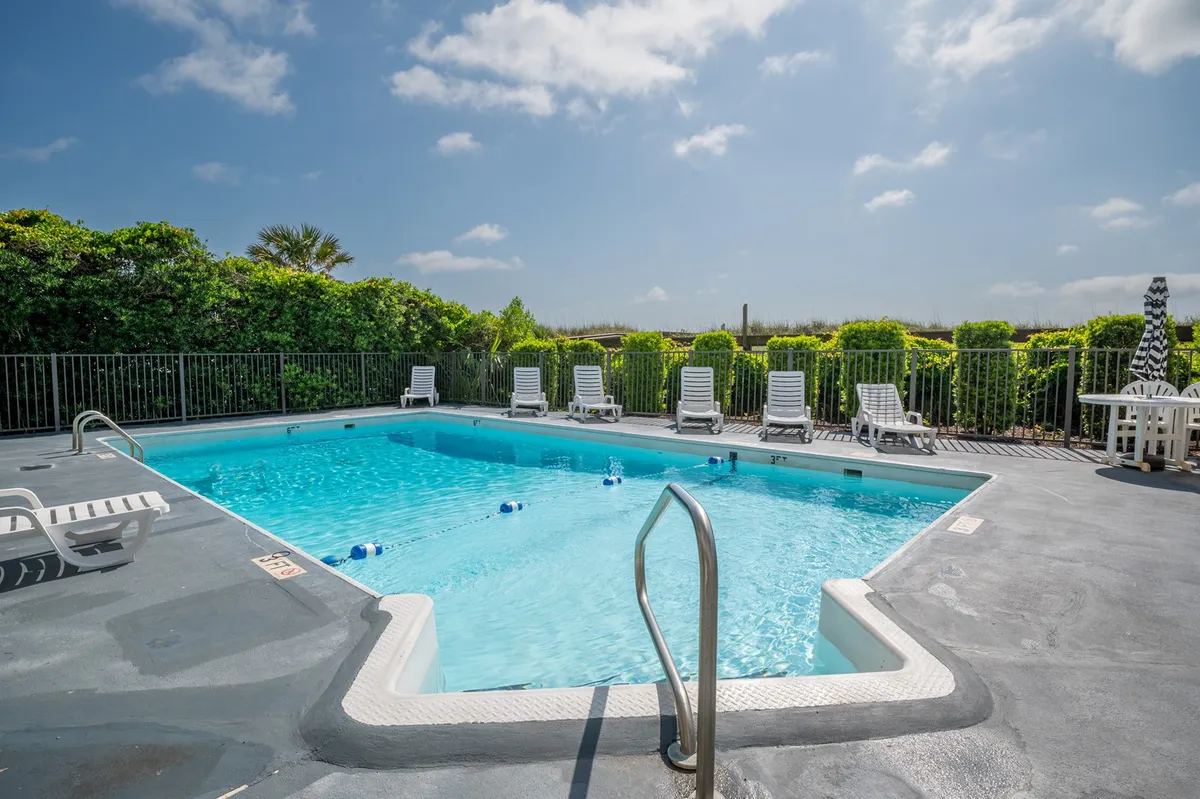 An inviting exterior shot of a sparkling swimming pool surrounded by lounge chairs and lush greenery. The tranquil setting is perfect for sunbathing, socializing, or enjoying a swim during Carolina Beach’s sunny summer months.