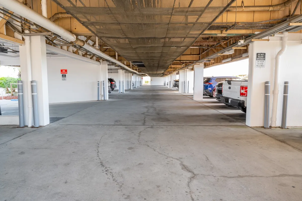A well-lit parking area with parked cars, structural columns, and clear pathways. The scene conveys ample, convenient parking that is easily accessible and practical for guests unloading luggage or groceries upon arrival.
