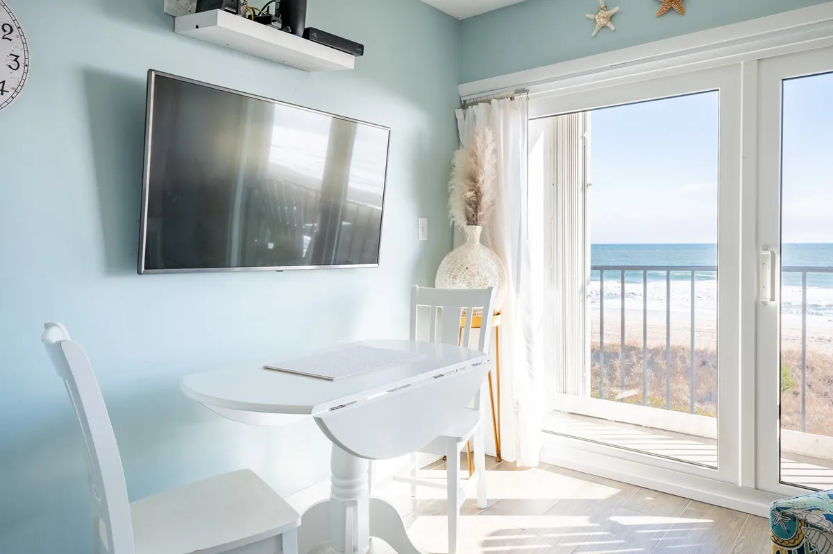 This interior view spotlights a bright dining area with a white table set near glass doors that offer a stunning ocean view. The setup is perfect for enjoying meals with natural light and a relaxing backdrop, making the dining nook feel connected to the surrounding coastal scenery.